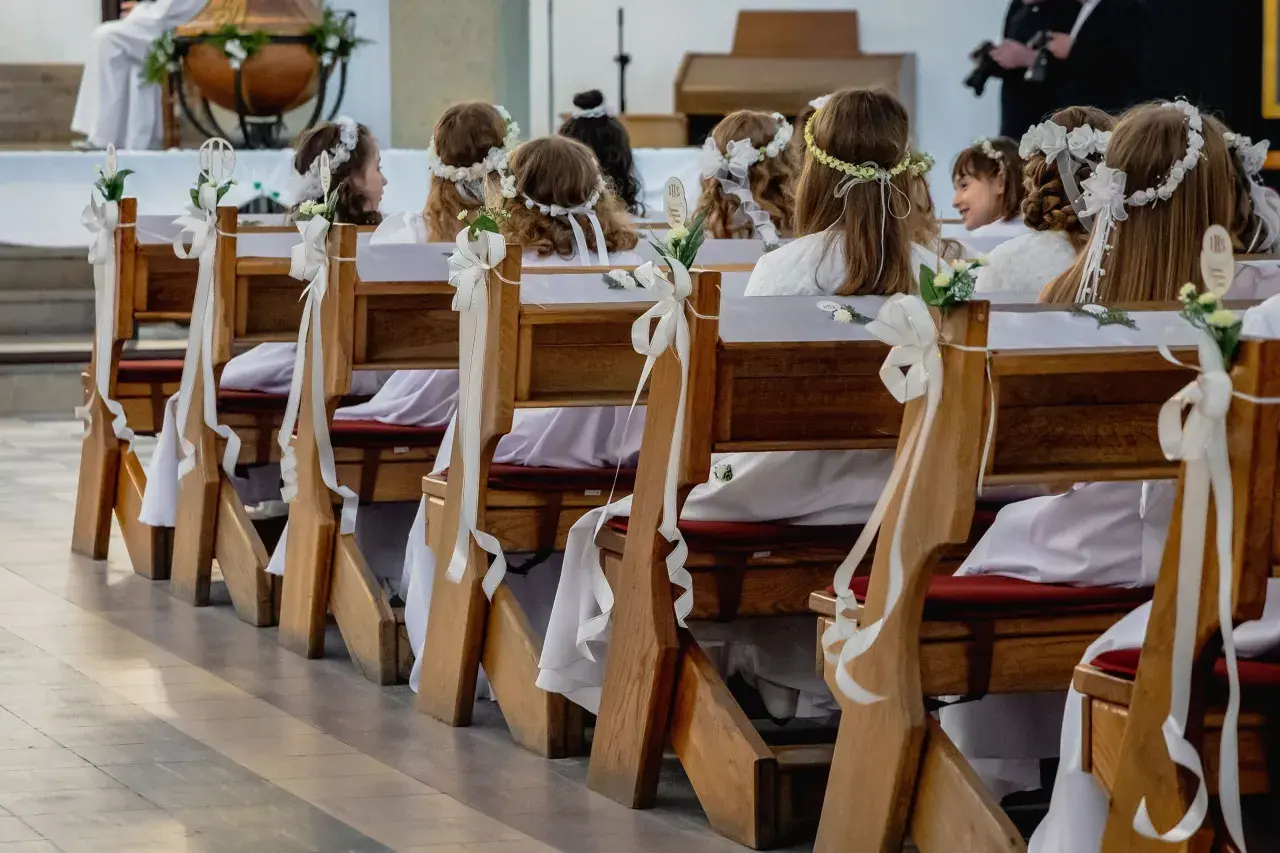 Dzieci w bieli, z wiankami na głowach, siedzą w ławkach kościelnych. Zastanawiasz się, ile trwaja komunie? To ważny dzień dla nich.