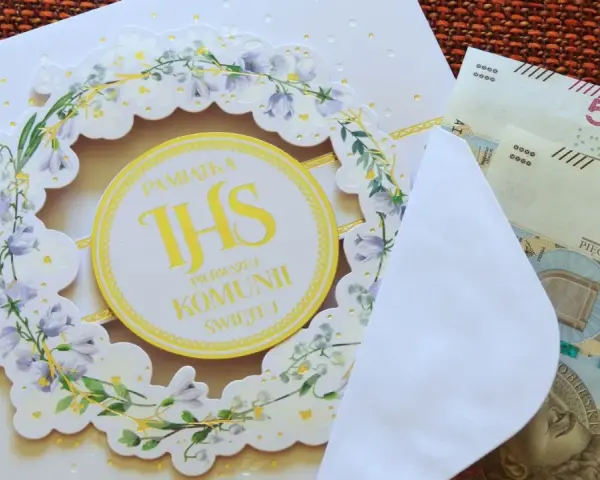 Biała kartka z motywem kwiatowym i napisem "Pamiątka Pierwszej Komunii Świętej", obok koperta z banknotami 500 zł.