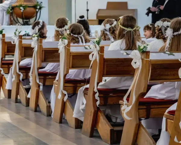 Dzieci w bieli, z wiankami na głowach, siedzą w ławkach kościelnych. Zastanawiasz się, ile trwaja komunie? To ważny dzień dla nich.