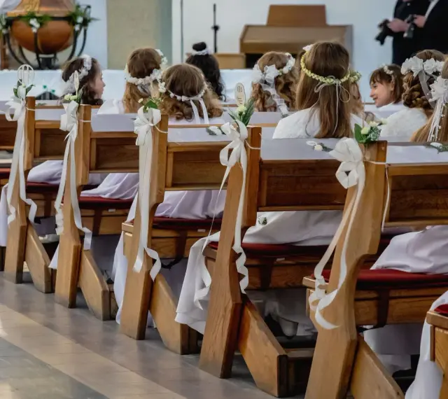 Dzieci w bieli, z wiankami na głowach, siedzą w ławkach kościelnych. Zastanawiasz się, ile trwaja komunie? To ważny dzień dla nich.