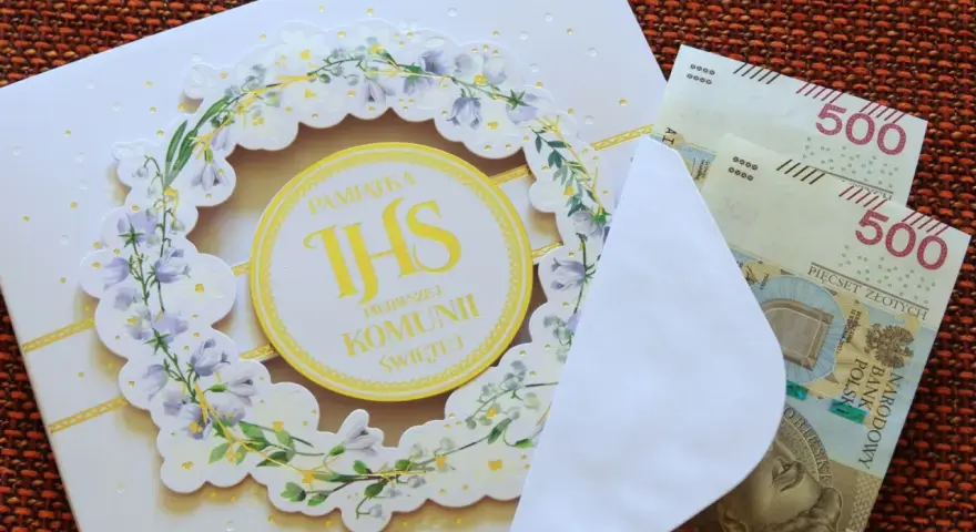 Biała kartka z motywem kwiatowym i napisem "Pamiątka Pierwszej Komunii Świętej", obok koperta z banknotami 500 zł.