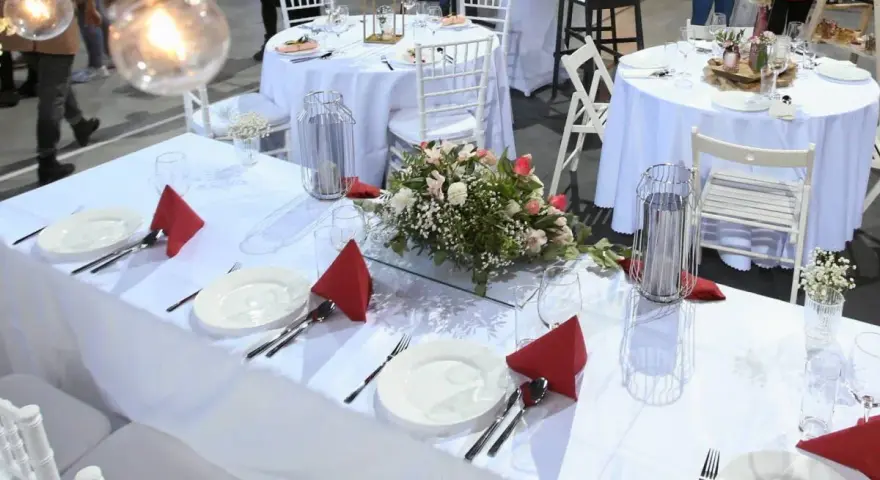 Elegancko nakryte stoły weselne z czerwonymi serwetkami i kwiatami. Zastanawiasz się, ile kosztuje uczesanie na wesele?